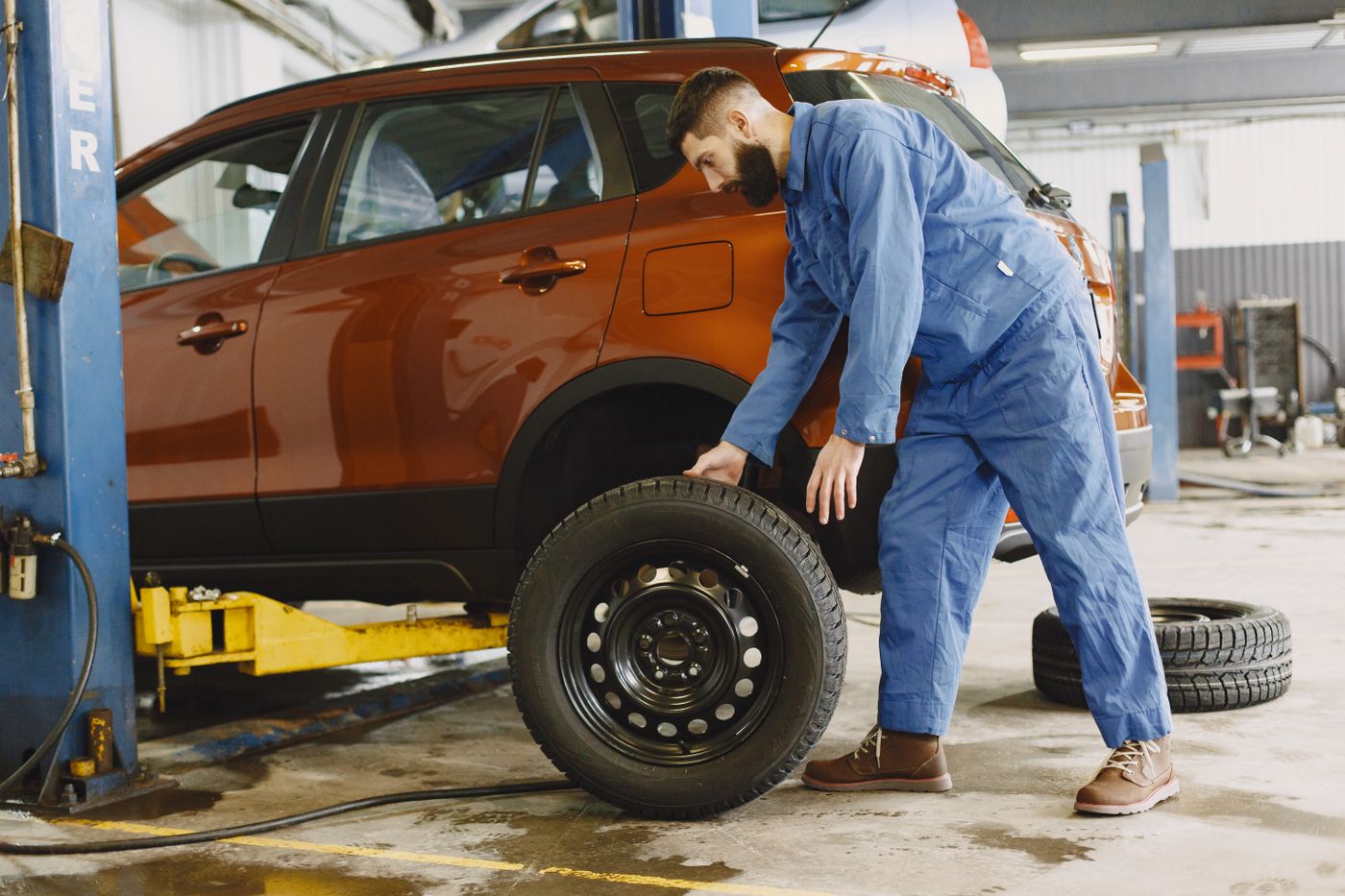 Technician rolling a fresh tire to a car on the lift
