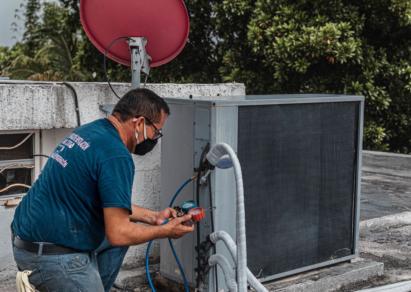 Copper State Air technician servicing a rooftop Carrier condenser unit with gauges