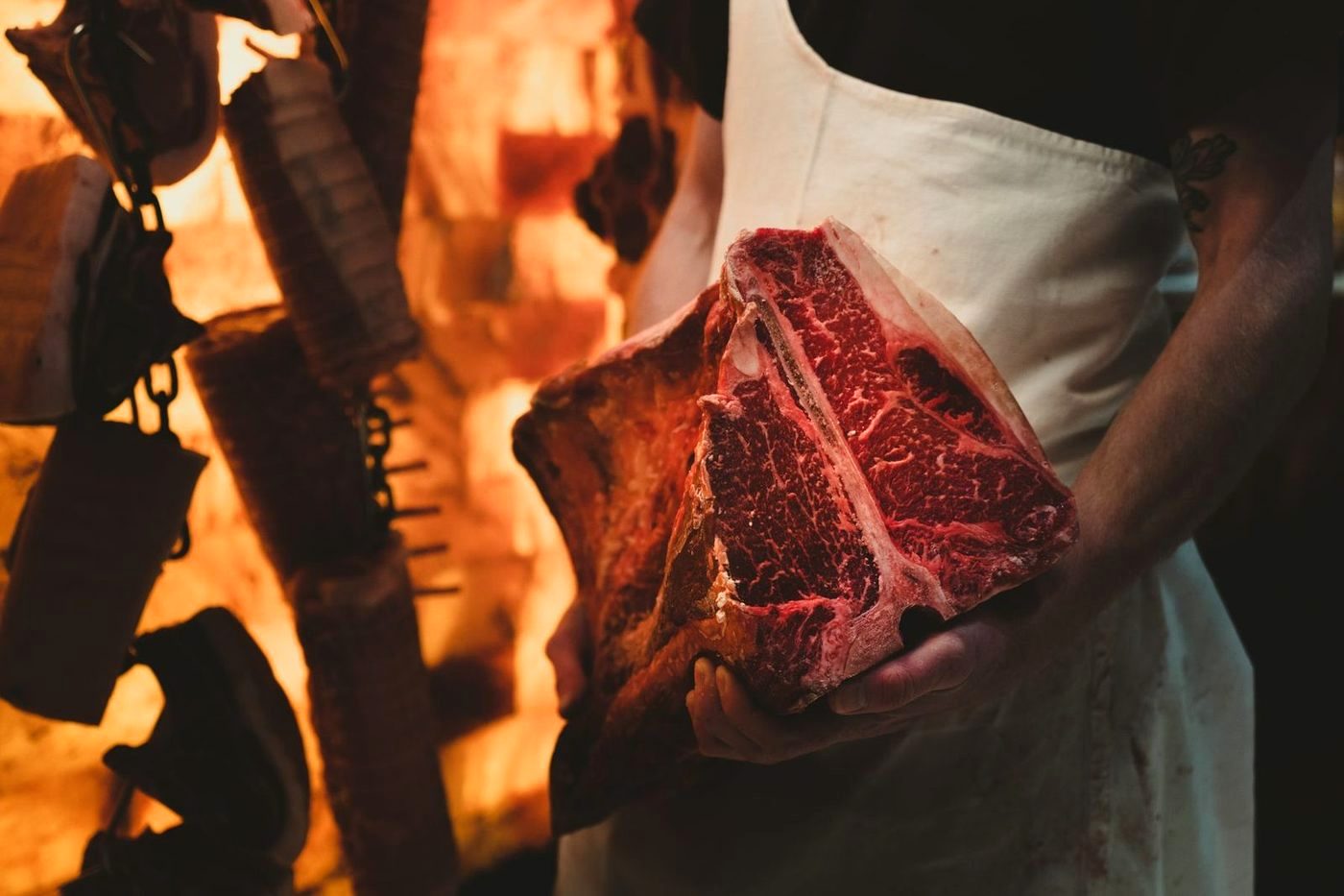 A butcher carrying a dry-aged porterhouse past the fire