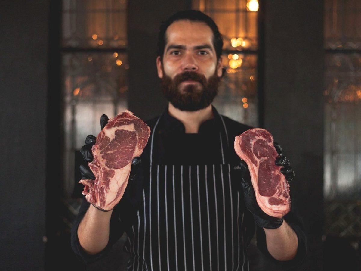 Third-generation owner and head butcher holding two ribeyes