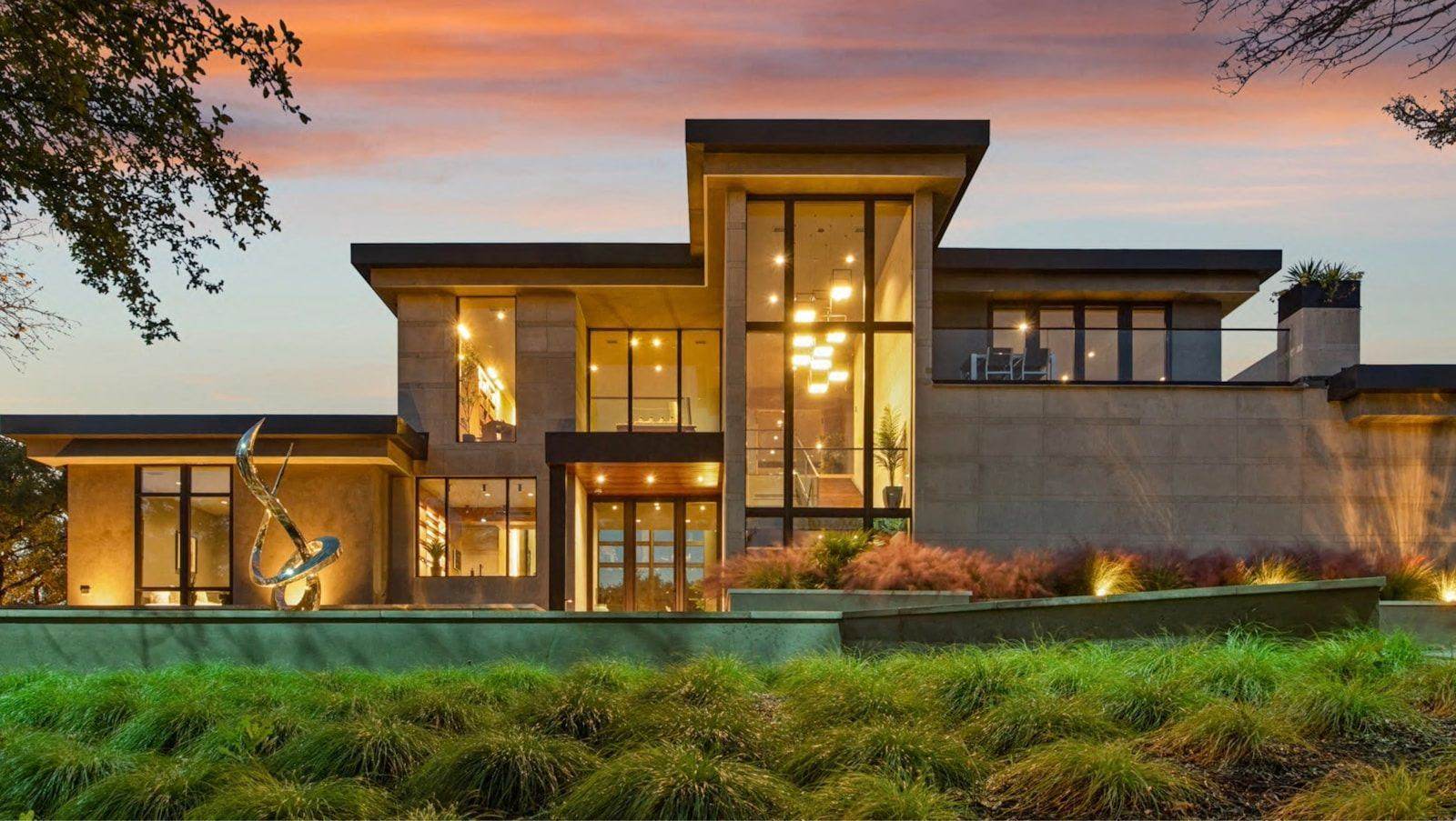 Modern luxury estate glowing at dusk, floor-to-ceiling glass and sculpture garden